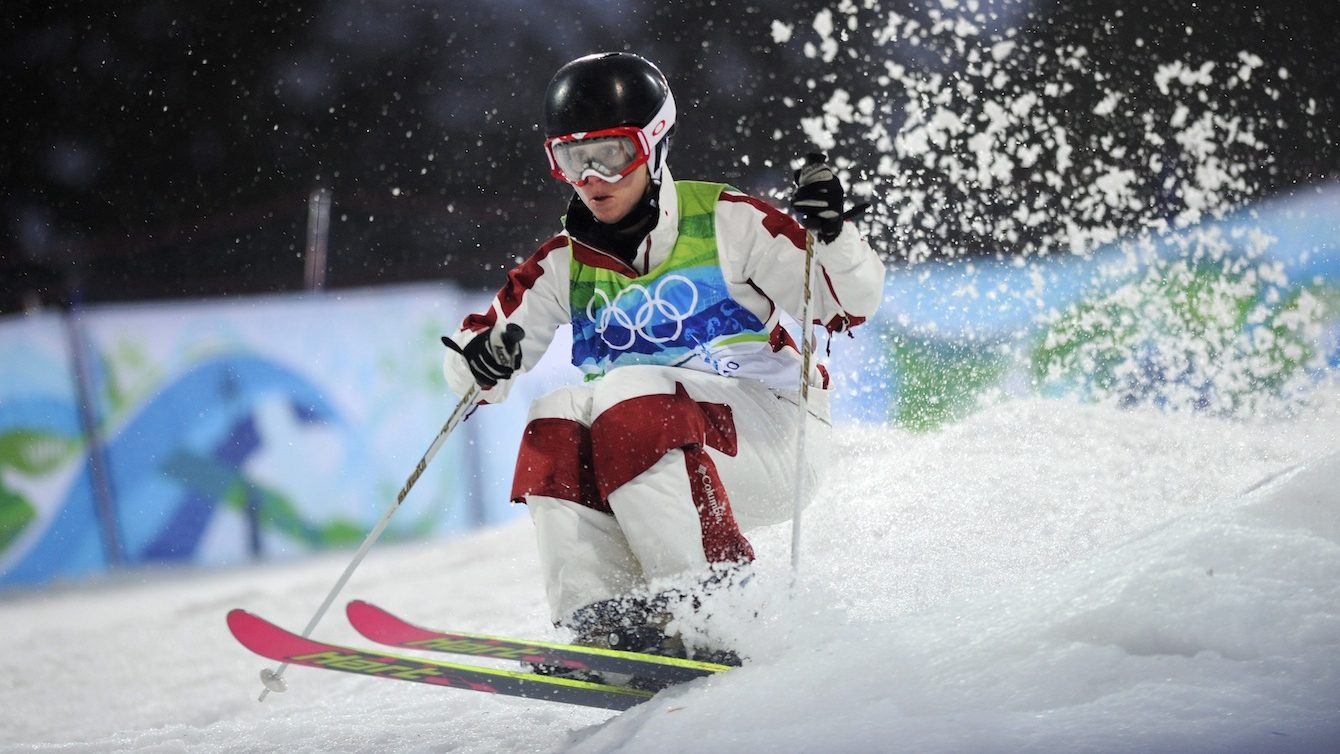 Jennifer Heil in a white snowsuit with red knee matches skis down a moguls course