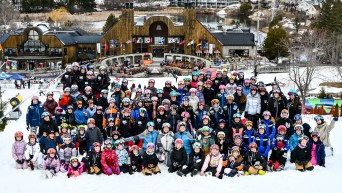 A large group of young female skiers cheer in front of a chalet