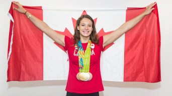 Penny Oleksiak, wearing a red t-shirt and four Olympic medals, holds up a Canadian flag.