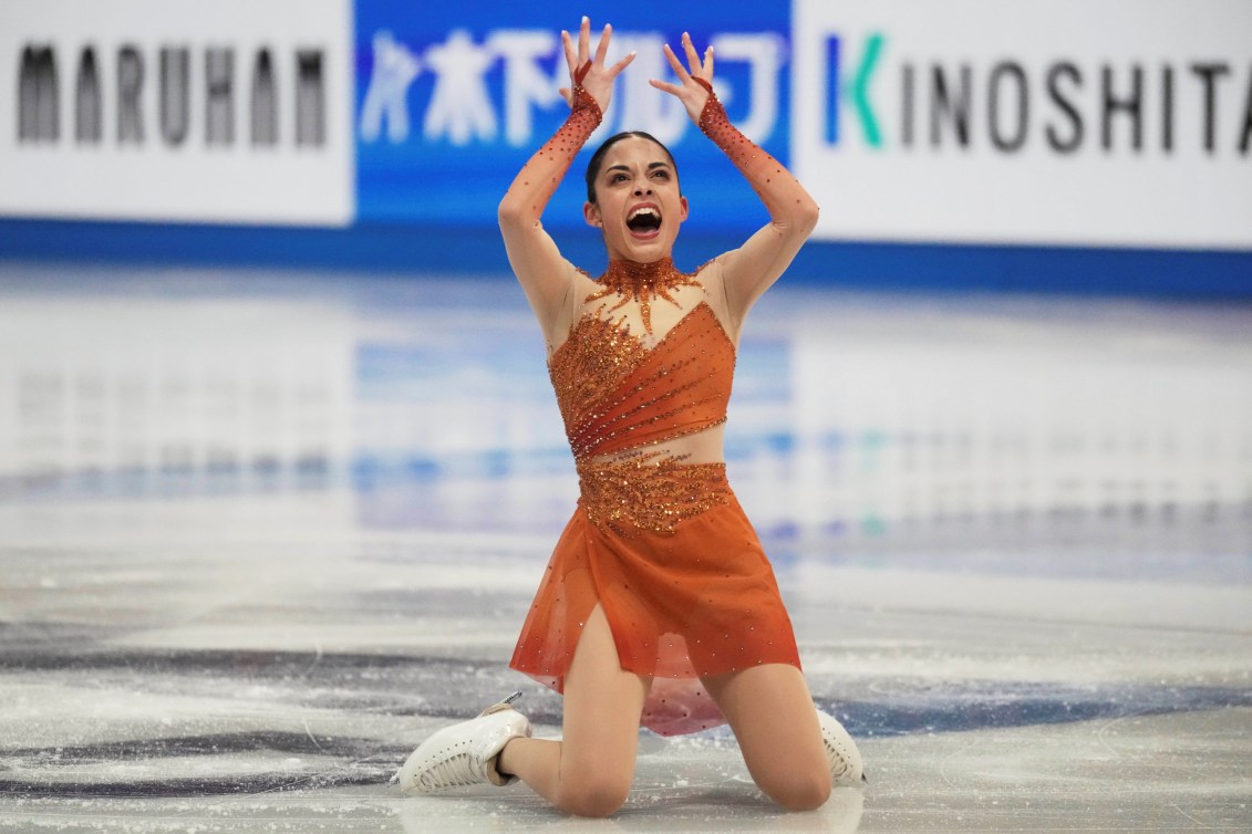 Madeline Schizas in an orange dress kneels on the ice in the middle of her routine