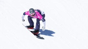Eliot Grondin crouches on his snowboard while wearing a pink singlet