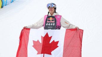 Liam Brearley holds a Canadian flag in front of his body in front of a snow hill